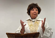 A woman wearing a white robe and standing at a podium. Description generated by AI