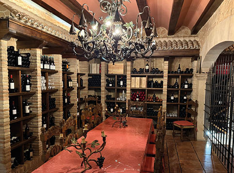A wine cellar with a long table and a chandelier. Description generated by AI