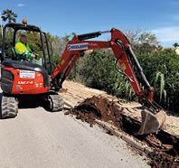 A red and black construction vehicle is digging up the road. Description generated by AI