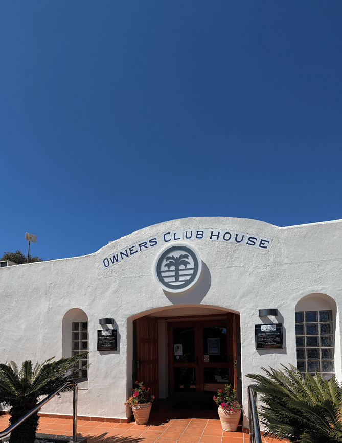 A white building with a blue sign that says Owner's Clubhouse. Description generated by AI
