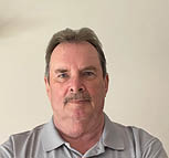A man wearing a gray shirt with a logo on it. Description generated by AI