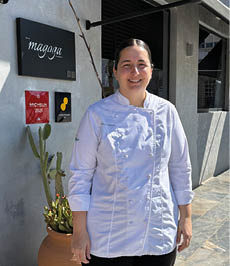 A woman wearing a white shirt and black pants standing in front of a building. Description generated by AI