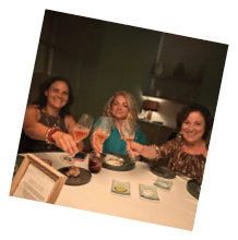 Three women sitting at a table with wine glasses. Description generated by AI