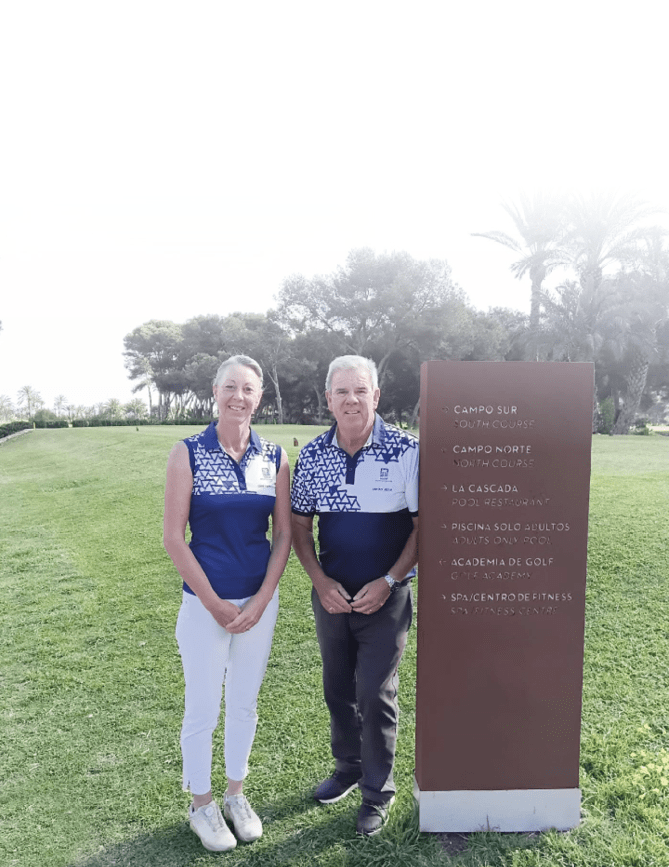 A man and a woman standing in front of a sign. Description generated by AI