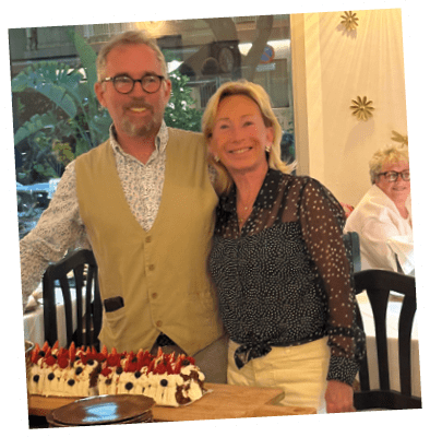 A man and woman standing in front of a table with a cake on it. Description generated by AI