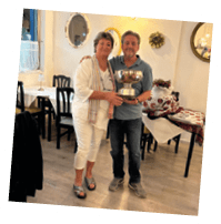 A man and woman standing in a restaurant holding a trophy. Description generated by AI