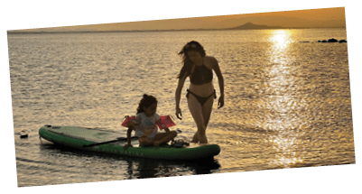 A woman and a child are on a green surfboard in the water. Description generated by AI