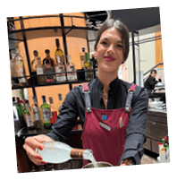 A woman in a black shirt and apron pouring a drink into a copper cup. Description generated by AI