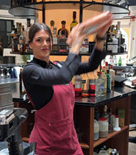 A woman wearing a red apron and a black shirt is standing in a bar. Description generated by AI