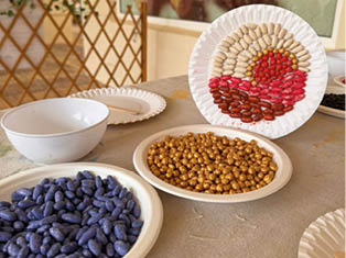 A table with a bowl of purple beans, a bowl of yellow beans, a plate of red beans, and a plate of brown beans. Description generated by AI