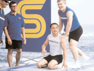 Four men are standing on a surfboard, with one man kneeling on the board. The other men are standing around the kneeling man, possibly posing for a picture. AI generated content