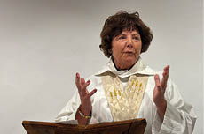 A woman wearing a white robe and standing at a podium. Description generated by AI