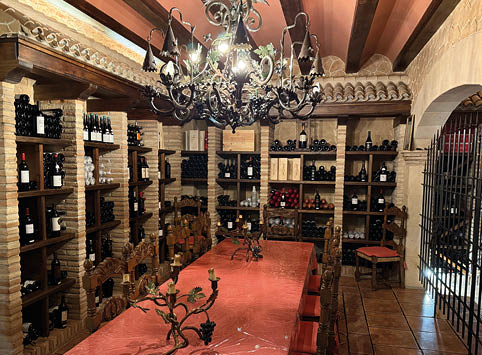 A wine cellar with a long table and a chandelier. Description generated by AI