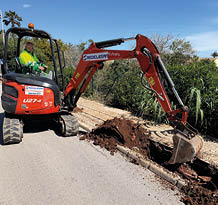 A red and black construction vehicle is digging up the road. Description generated by AI