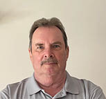 A man wearing a gray shirt with a logo on it. Description generated by AI