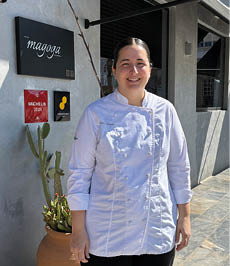 A woman wearing a white shirt and black pants standing in front of a building. Description generated by AI