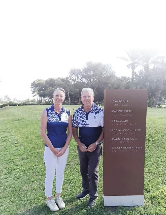 A man and a woman standing in front of a sign. Description generated by AI