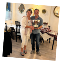 A man and woman standing in a restaurant holding a trophy. Description generated by AI