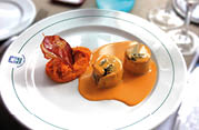 A white plate holds two pieces of food covered in orange sauce next to a dollop of mashed orange puree topped with a crispy garnish. Description generated by AI