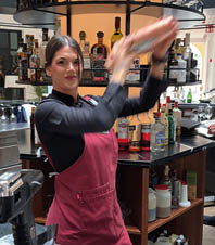 A woman wearing a red apron and a black shirt is standing in a bar. Description generated by AI