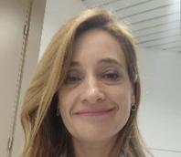 A woman wearing a white jacket and a pink lipstick smiling. Description generated by AI