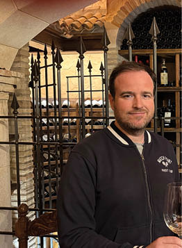 Two men standing in front of a wine cellar. Description generated by AI