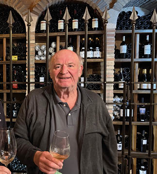 Two men standing in front of a wine cellar. Description generated by AI