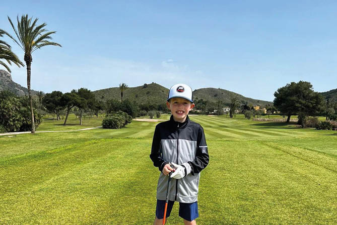 A young boy is standing on a golf course holding a golf club. Description generated by AI