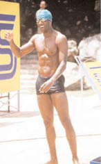 A man wearing a blue swim cap and black swim trunks stands on a diving board. AI generated content