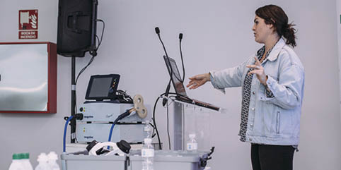 A woman standing in front of a laptop. Description generated by AI