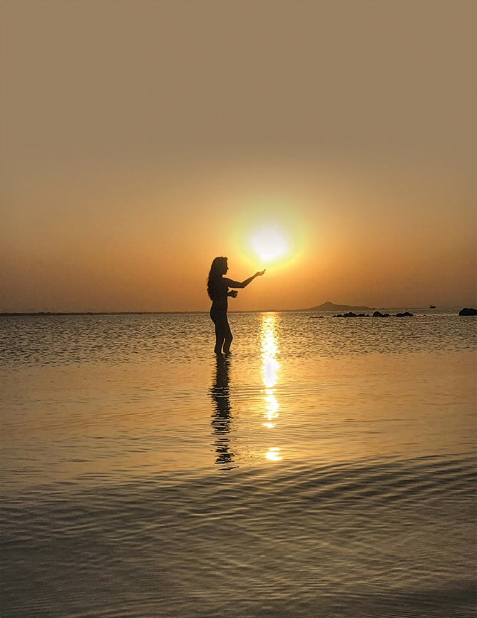 A woman standing in the water at sunset. Description generated by AI