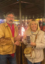 A man and woman standing in front of a fire. Description generated by AI