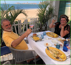 A man and woman are sitting at a table with food and drinks. Description generated by AI