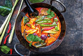 Traditional Thai kaeng phet red curry with vegetables as top view in a wok with copy space right